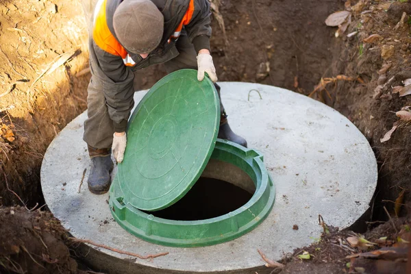 En arbetare monterar ett avloppshål på en septiktank av betongringar. Byggande av avloppsnät för hus på landet — Stockfoto