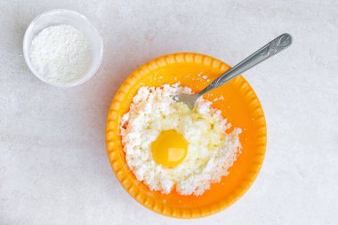 Cheesecake pişiriyorum. Masanın üzerinde taze süzme peynir ve yumurtalı sarı bir fincan var. Yanında da un dolu bir bardak.