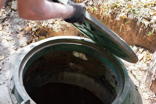 Adam kanalizasyon kapağını açıyor. Septik tank denetimi ve bakımı.