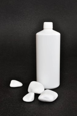 Siyah arka planda taşlarla süslenmiş sağlıklı ürün için beyaz plastik bir şişe. 