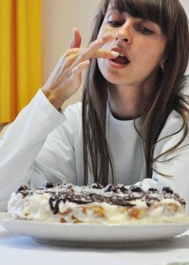 Beautiful girl tastes freshly baked cake licking fingers clipart
