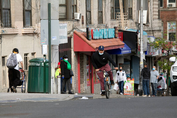 BRONX, NEW YORK/USA - March 8, 2020: Young Latino wearing mask rides bike on uphill street. 