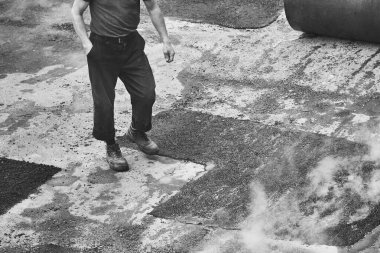 İşçi adam yeni tüten asfalt üzerinde yürüyor. siyah ve beyaz fotoğrafçılık