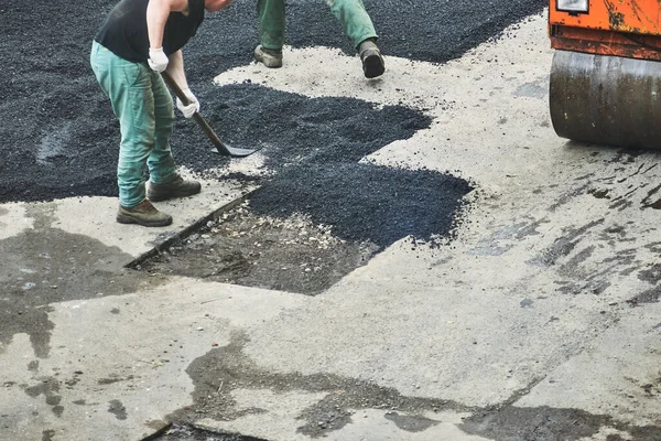 İşçi bir kürekle asfalt serer.