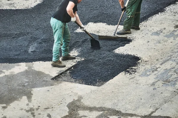 İşçiler yolu onarıyor. İnsan tarafından asfalt döşeme. Adam kürekle zümrüt atıyor.