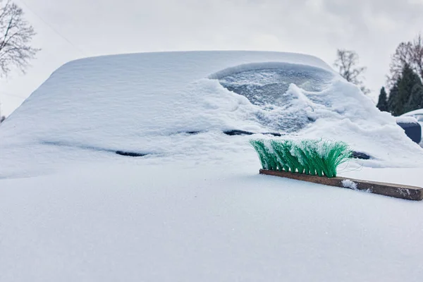 green snow brush lies on the hood of a snow-covered car
