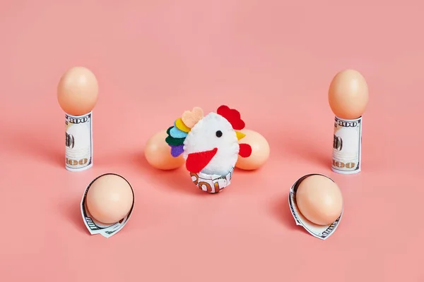toy chicken and eggshells with 100 dollar bills. concept. pink background