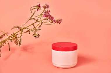 Üzerinde yazı olmayan pembe bir kavanoz. Kırmızı çiçek kabuğunun arka planında. konsept kozmetik cilt bakımı