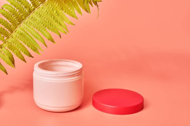 Pembe arka planda yeşil eğreltiotu yaprağı. Krema kavanozu. Kozmetik bakım. Boşluğu kopyala