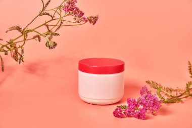 Üzerinde yazı olmayan pembe bir kavanoz. Kırmızı çiçek kabuğunun arka planında. konsept kozmetik cilt bakımı