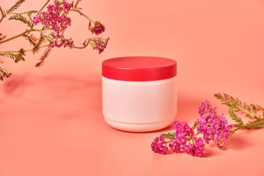 Üzerinde yazı olmayan pembe bir kavanoz. Kırmızı çiçek kabuğunun arka planında. konsept kozmetik cilt bakımı