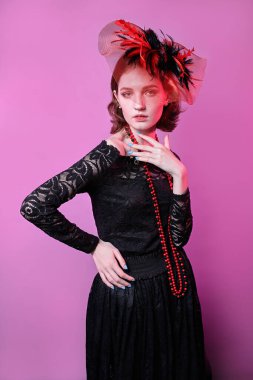 Şapkalı ve siyah elbiseli genç bir kızın şık portresi. pembe arkaplan