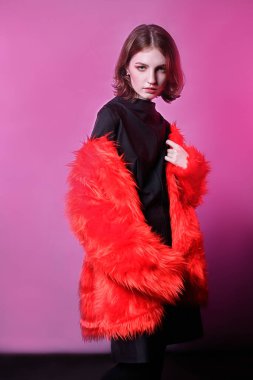 Kırmızı kürk manto giyen kızıl saçlı genç kız. pembe arkaplan