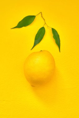 Sarı arka planda yeşil yapraklı olgun bir limon. Düz yat. en üstteki görünüm