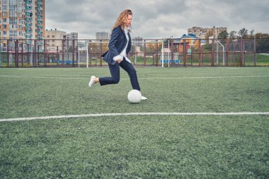 Takım elbiseli bir kız stadyum sahasında futbol topuna vuruyor. konsept