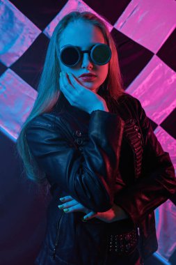 Yarış gözlüklü, deri ceketli neon ışıklı kızın portresi bitiş bayrağının arka planında