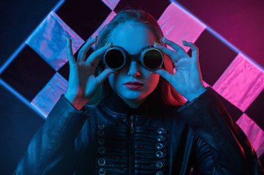 Yarış gözlüklü, deri ceketli neon ışıklı kızın portresi bitiş bayrağının arka planında