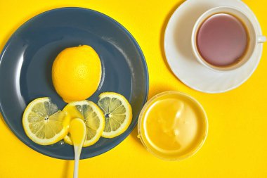 Mavi tabakta dilimlenmiş taze limon. Sarı masada çay ve bal var.