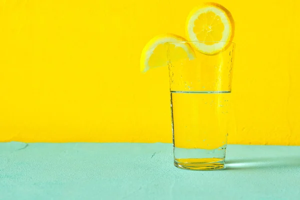 Sarı zemin üzerinde limon dilimleri olan bir bardak su.