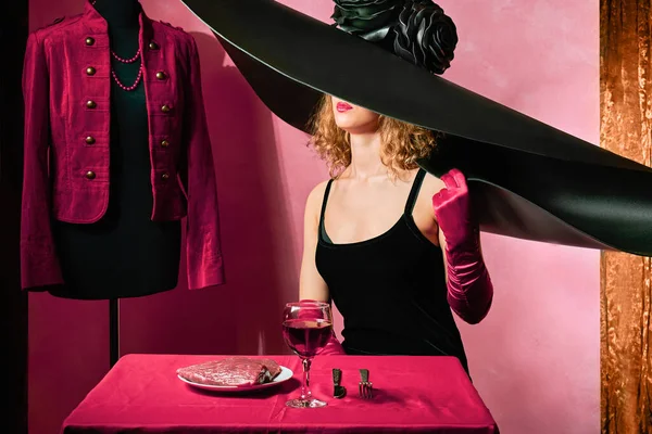 大きな帽子をかぶったグラマラスモデルの女性と生肉の食事とテーブルの赤い手袋 — ストック写真