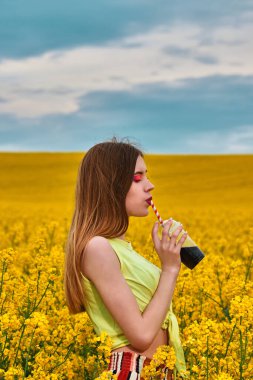 Genç kız tarlada içki içiyor.