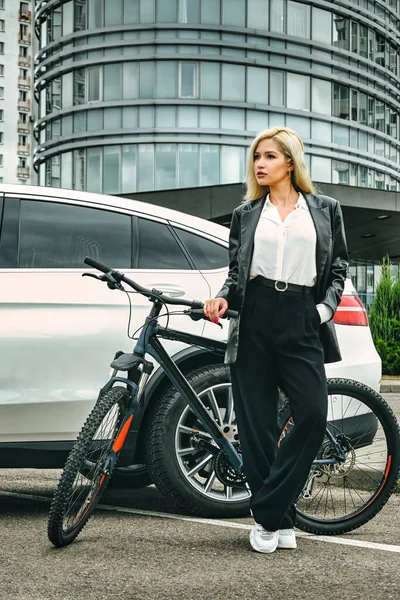 business portrait of girl on a bicycle on the background of an expensive car. concept
