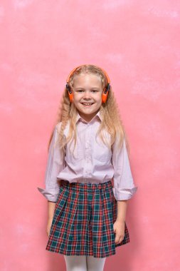 Kulaklıklı küçük bir kızın portresi. Üniformalı kız öğrenci. pembe arkaplan