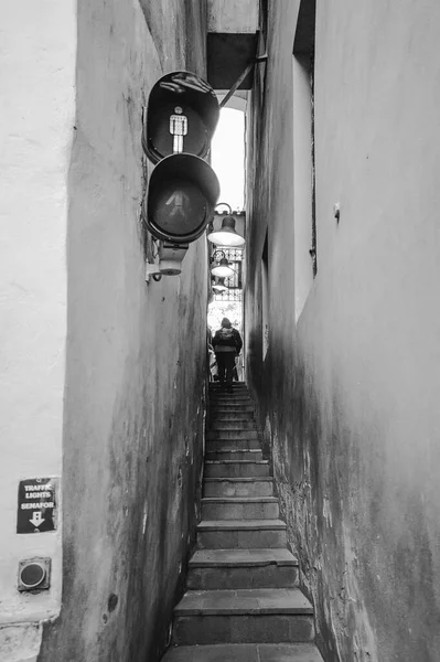 White and black  photo. This is the narrowest street in Prague. A special traffic light has been installed for people. A traffic light is needed because two people cannot disperse on this street.