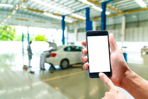 Hand hold smartphone with car repair service center background blur — Stock Photo, Image