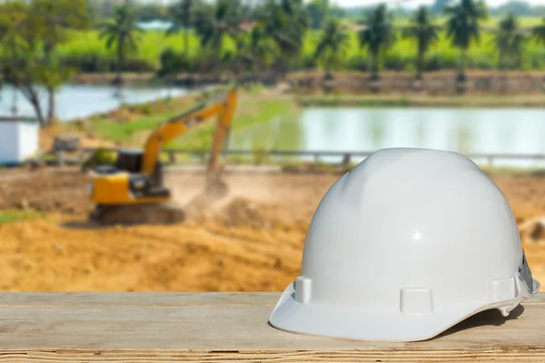 Engenharia de segurança e um capacete descansando sobre os detalhes do canteiro de obras com uma escavadeira — Fotografia de Stock