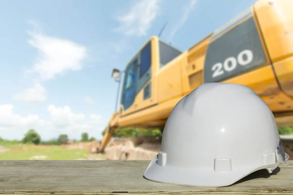 Veiligheidstechniek en een helm die rusten op de details van de bouwplaats met een bulldozer achter hen. — Stockfoto
