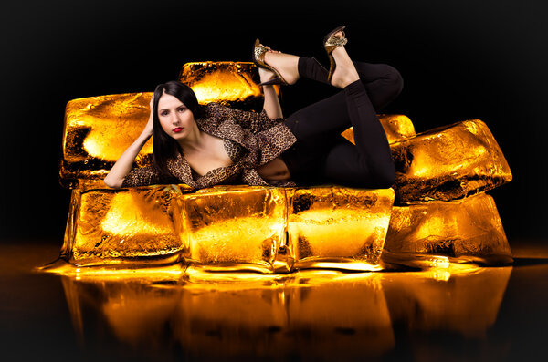 Portrait of a young beautiful sexy woman in a leopard clothes, lying on gold bullion