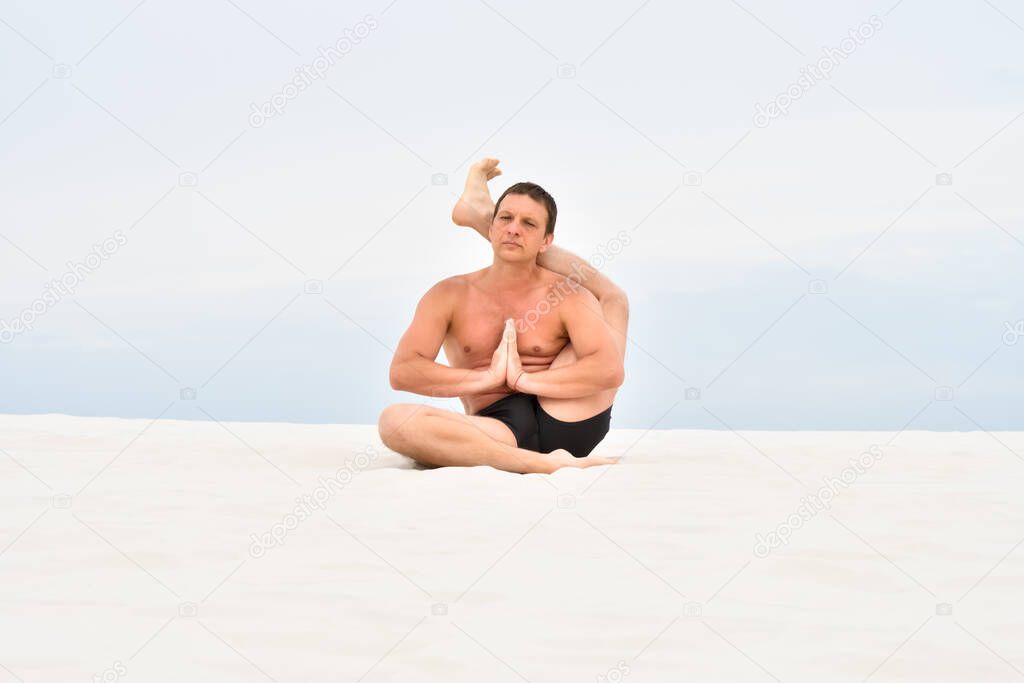 Young man sitting with foot behind his head on the beach