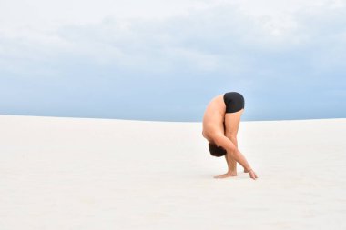 Genç adam yoga yapıyor Uttanasana sahilde poz veriyor