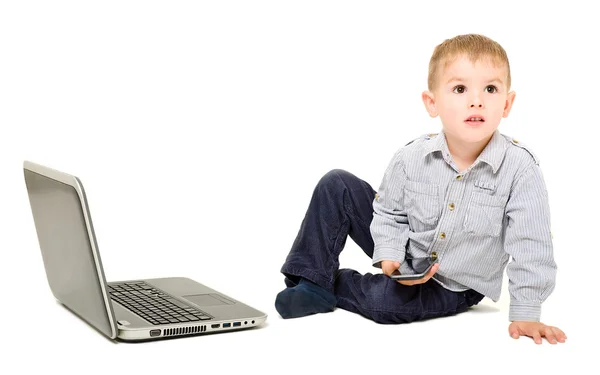 Niño con teléfono en la mano sentado cerca de la computadora portátil — Foto de Stock