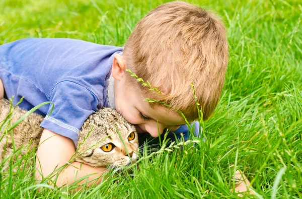Веселий хлопчик обіймає кота, що лежить на траві — стокове фото