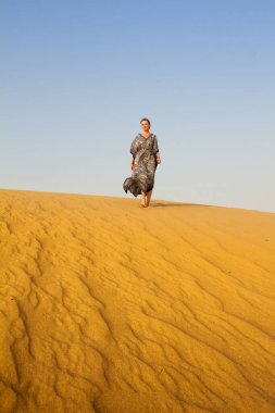 Genç bir kadın güneşli bir yaz gününde beyaz kumda yürüyor, tatil konsepti.