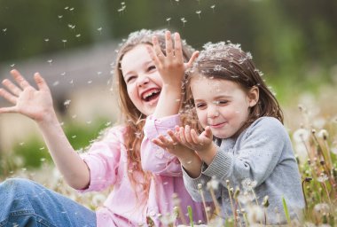 İki tatlı çocuk karahindibanın arasında oturmuş karahindiba üflüyor.