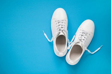 Mavi arka planda bir çift beyaz deri spor ayakkabı.. 