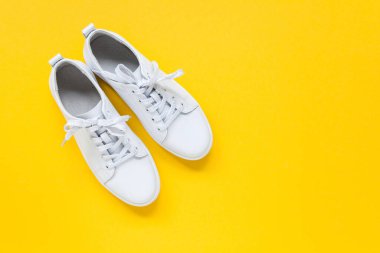 Sarı arka planda beyaz deri bir çift spor ayakkabı. Boşluğu kopyala