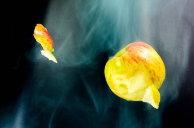 Çırpınan elma, patlamada hasar görmüş. Siyah arka planda yeşil-kırmızı elma. Yeşil ve beyaz duman yükseliyor. 