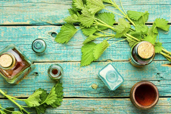 ガラス瓶や新鮮なイラクサの葉にエッセンス油を入れます 木製のテーブルの上にウルティカのディオイカや純茎 薬用植物 — ストック写真