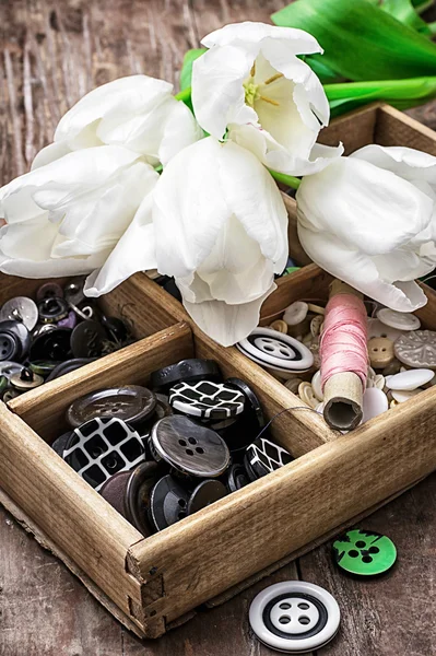 Sewing buttons against background of bouquet of white tulips — Stock Photo, Image