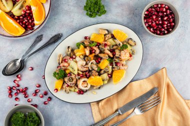 Plate with salad of mussels, squid, shrimp with kiwi fruit, pomegranate seeds and orange. Flat lay.