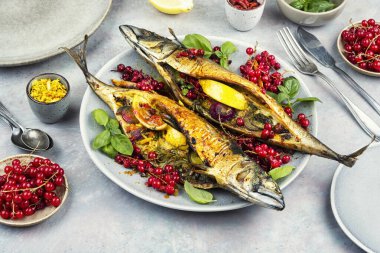 Limonlu ızgara uskumru, otlar ve kırmızı frenk üzümü tabakta servis ediliyor. Taze malzemeli leziz kızarmış balık yemeği, sağlıklı yemek ve gurme mutfağı için mükemmel..