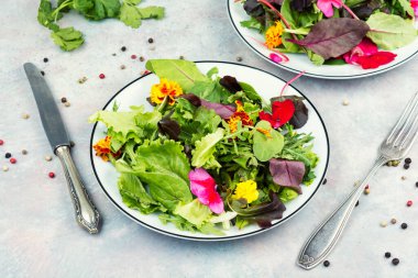 The salad consists of a mix of green and purple leafy vegetables, along with several colorful edible flowers in shades of yellow, red, and pink.