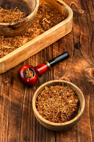 Ahşap yüzeyde kurumuş tütün yapraklarıyla dolu zarif tütün piposu. Rahatlama kavramı, sigara piposu.