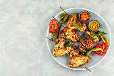 Ahşap şişte servis edilen ızgara tavuk kanatları ve bir tabakta sunuluyor. Boşluğu kopyala.