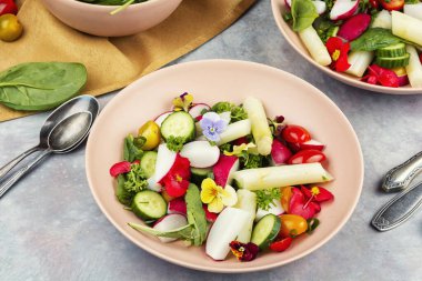 Beyaz kuşkonmaz ile sulu, yeşil bir salata. Karışık sebzeler, taze otlar ve yenilebilir çiçeklerle süslenmiş bir tabakta..