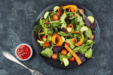 Taze bahar yeşillikleri, taze sebzeler ve bir tabakta sıralanmış şifalı otlar. Üst görünüm.
